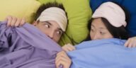 An interracial couple wearing sleep masks lying down on colorful pillows, portraying relaxation and rest.