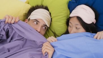 An interracial couple wearing sleep masks lying down on colorful pillows, portraying relaxation and rest.