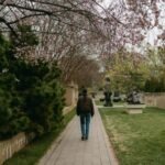 Woman walking under blooming trees in a sculpture garden during spring.