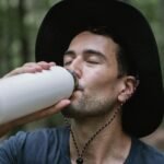 Close-up of a man drinking from a water bottle in a forest setting, capturing a refreshing moment outdoors.