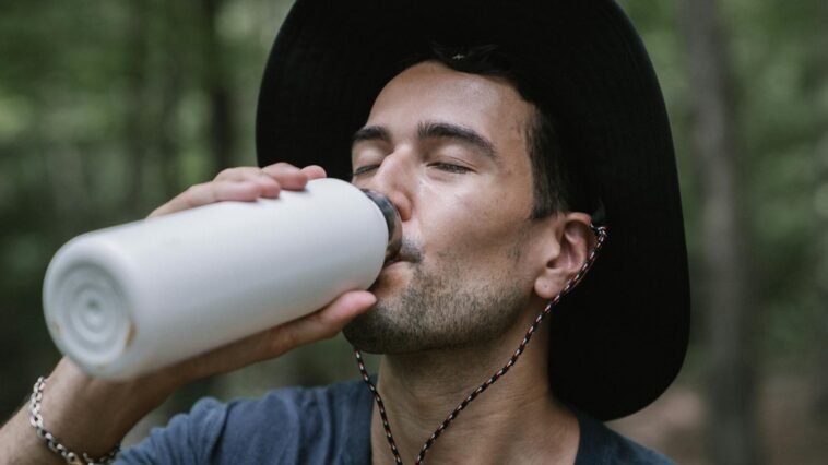 Close-up of a man drinking from a water bottle in a forest setting, capturing a refreshing moment outdoors.