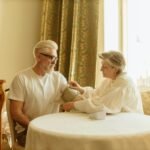 An elderly couple checks blood pressure using a digital monitor at their home table.