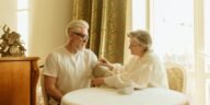 An elderly couple checks blood pressure using a digital monitor at their home table.