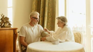 An elderly couple checks blood pressure using a digital monitor at their home table.